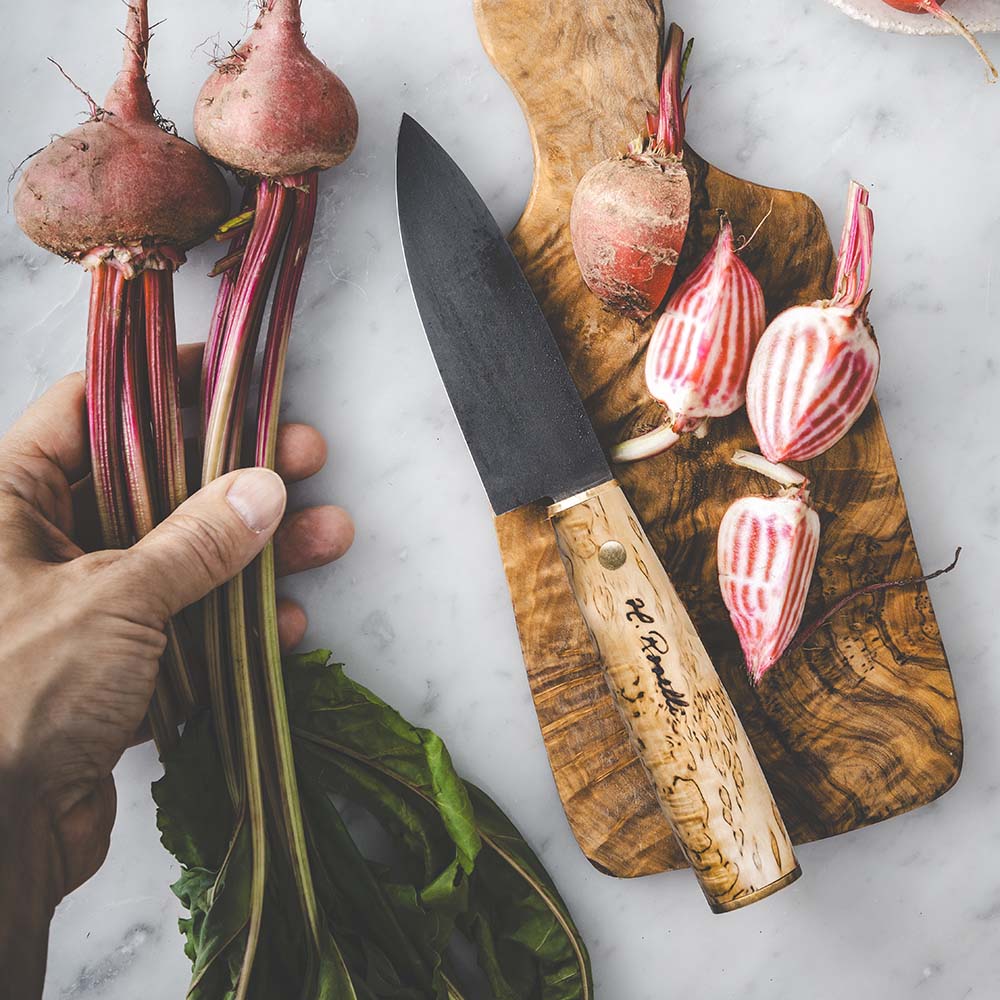 Roselli's finska handgjorda japanska kökskniv i modell "Allround-kniv". Med blad av kolstål och handtag av masurbjörk. Levereras med ett handgjort fodral av finskt naturgarvat läder.