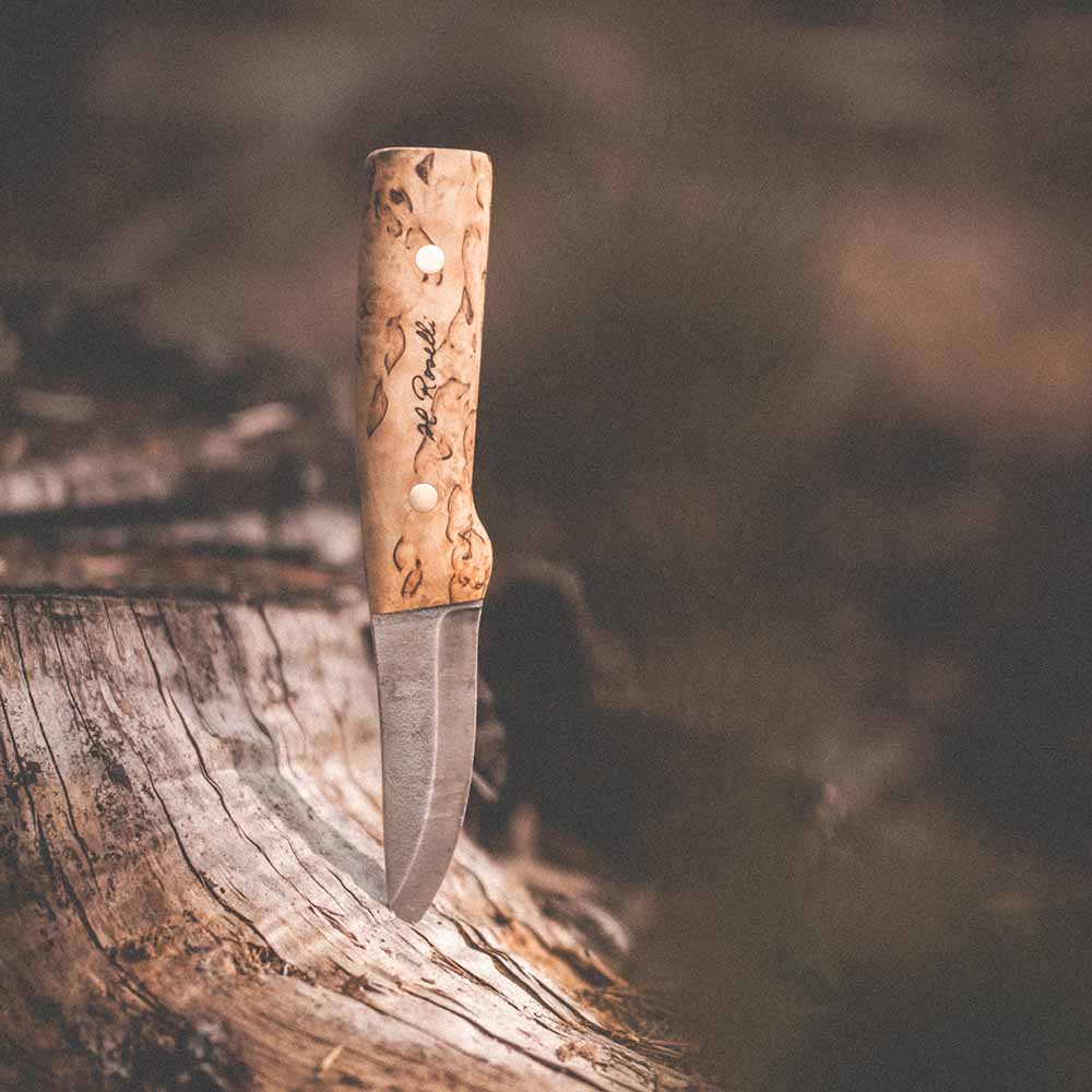 Rosellis handgjorda finska kniv i modellen "Hunting knife fulltånge" med handtag gjord av ljus masurbjörk ute i skogen